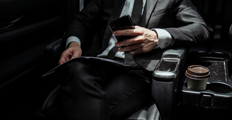 Businessman,On,Black,Suit,Sittin,In,A,Car,Holding,Smartphone