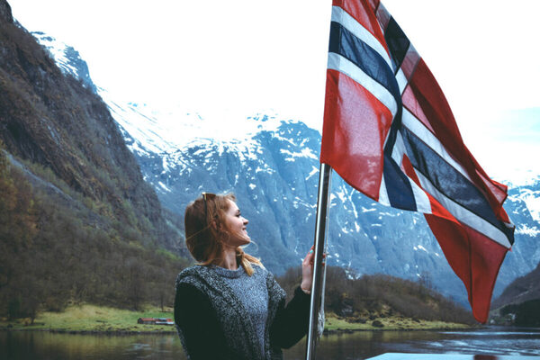 Tourist girl with flag of Norway enjoys beautiful view of fjord and mountains